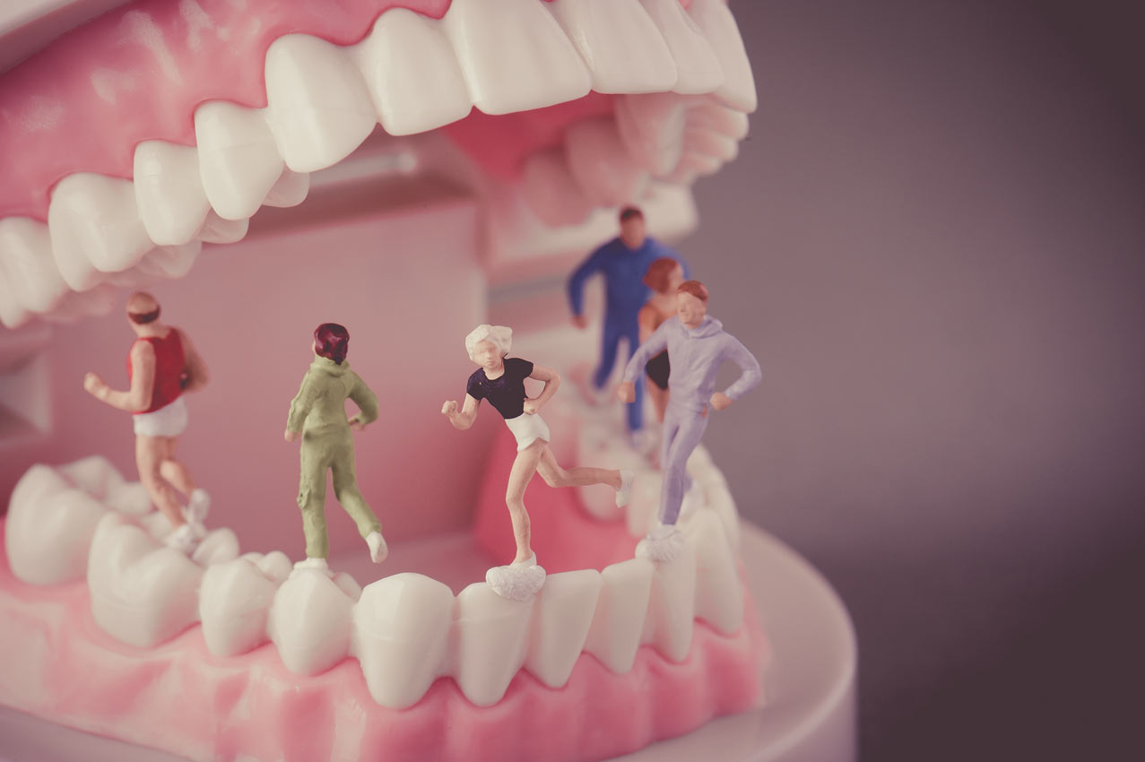 Miniature runner figurines jogging along the bottom teeth of a giant open dental mouth model