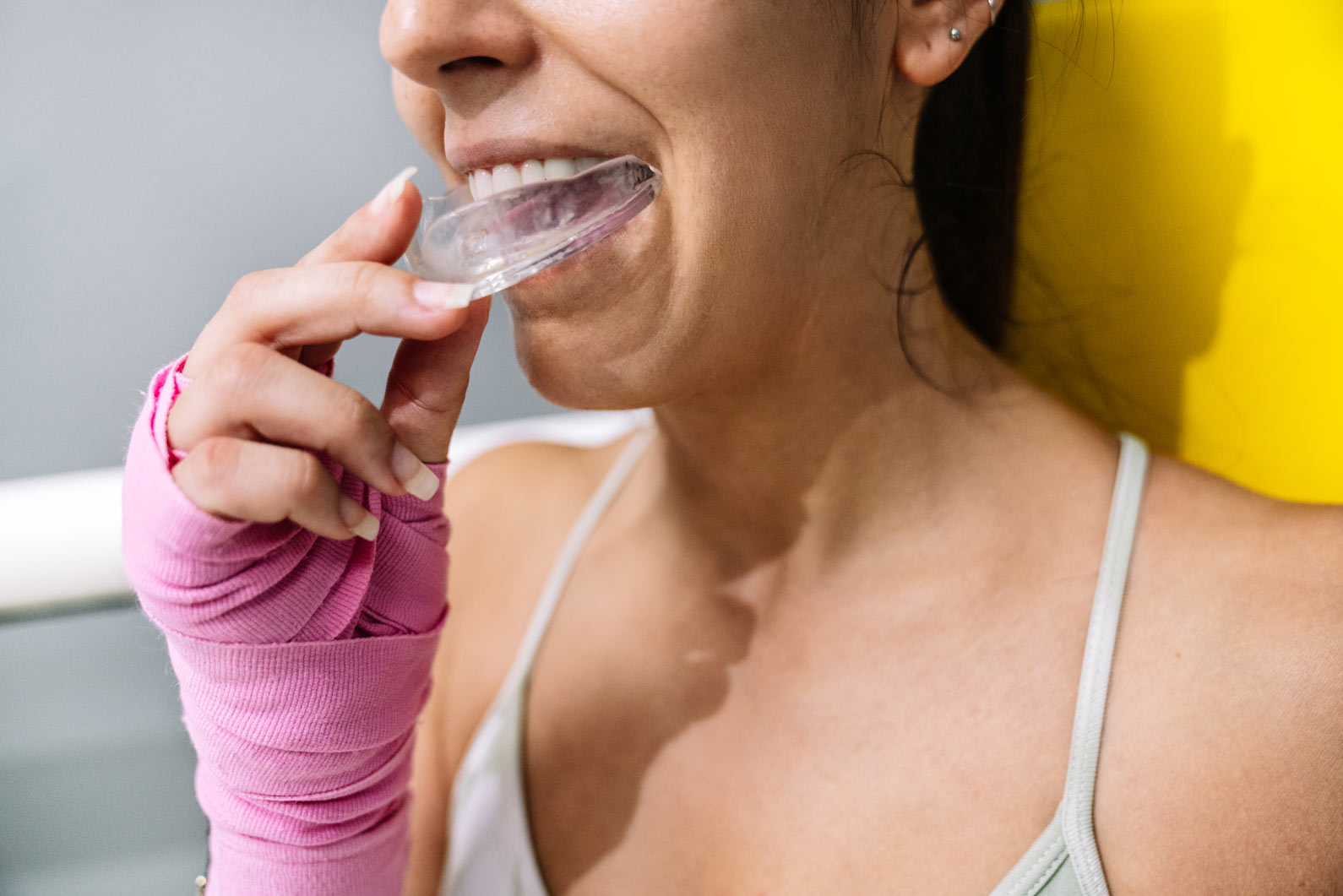 Female boxer with wrapped pink hands placing a clear protective mouthguard into her teeth