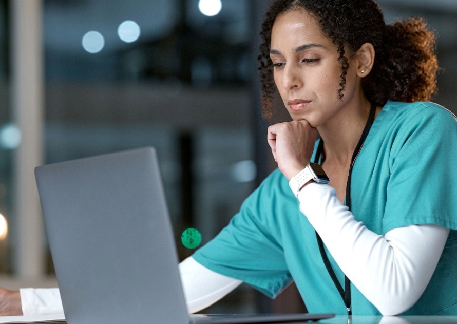 Enfermera con uniforme verde trabajando en ordenador portátil y tomando notas en oficina médica