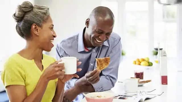 Une femme qui boit du café et un homme qui mange une tartine en souriant