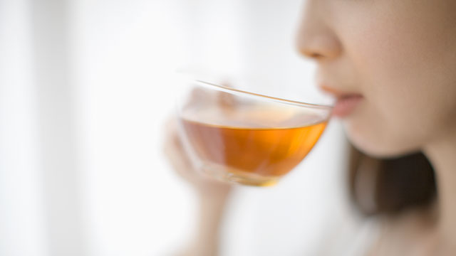 A woman is drinking tea from glass cup