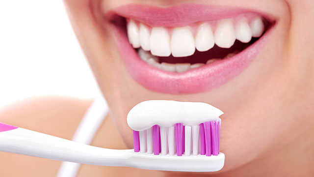 A close up of the toothpaste on toothbrush and woman's mouth