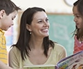 a teacher smiling showing a book to a group of children