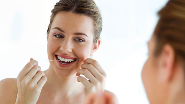 Woman with braces flossing her teeth – tips on how to stop bleeding gums with proper dental hygiene.
