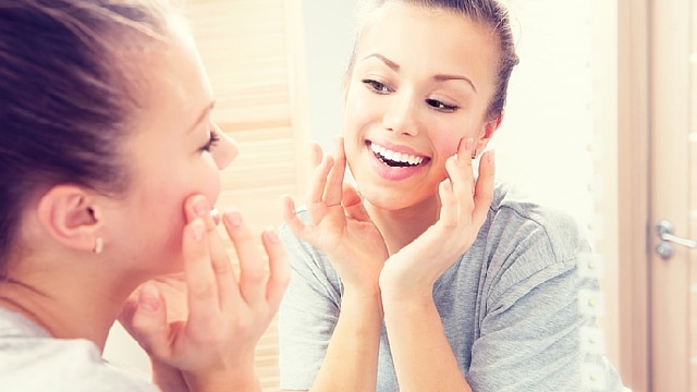 woman looking at the mirror smiling with her hands on her cheek