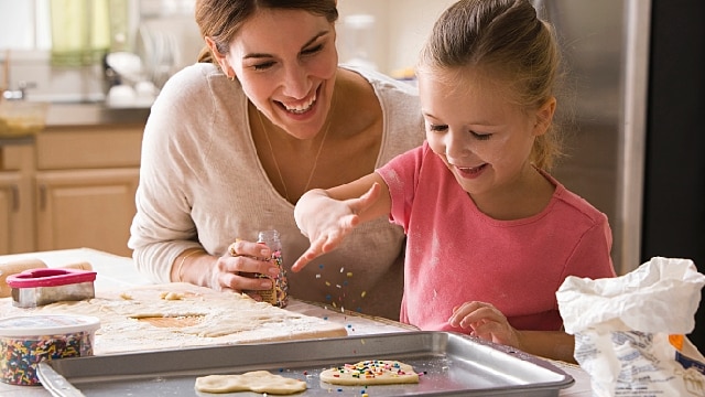 A young girl is baking cookies with her mother in the kitchen