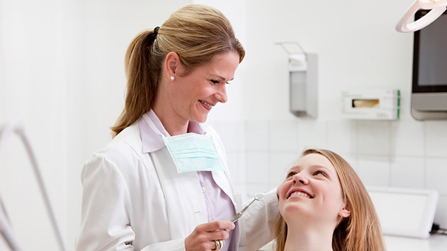 Female dentist in blue scrubs showing x-rays to patient, smiling young man.