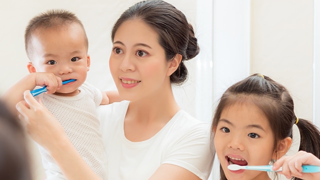 Una madre y sus dos hijo que se cepillan los dientes en el baño