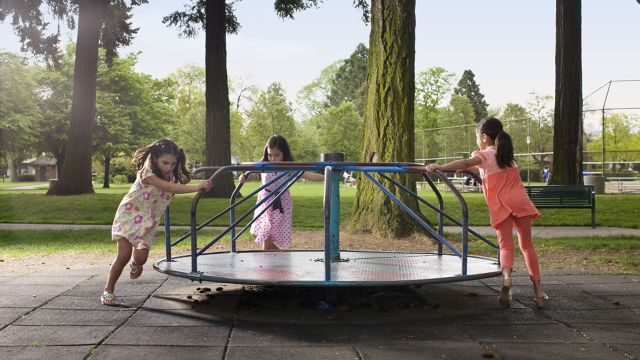 three girls running around a merry go round at the playground