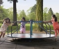three girls running around a merry go round at the playground