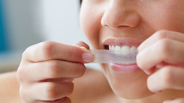 Mujer aplicando una tira blanqueadora de dientes