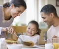 Family eating breakfast together in the morning with the mom serving the child in the middle a pancake as the mom, child and father smile