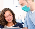 A male dentist is talking to the female patient in dental office