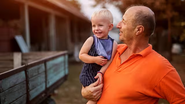 A proud grandfather holding his grandson while looking at him outdoors