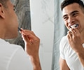 Young smiling man brushing teeth in a bathroom