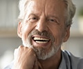 A senior man with gray hair and beard smiling with dentures