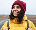 A woman with a backpack wearing yellow jacket and red hat stands on the road