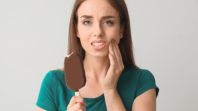 Mujer joven con dolor de dientes mientras come un helado