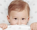 Child in a bed covering his lip with the blanket