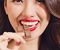 close-up of a young  woman wearing red lipstick and eating chocolate