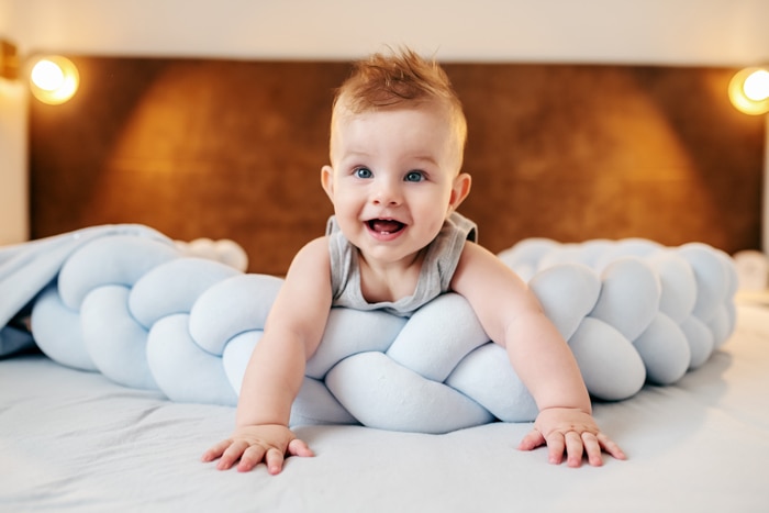 Adorable bebé caucásico sonriente acostado boca abajo en la cama en el dormitorio y mirando hacia arriba. El bebé tiene dos dientes.
