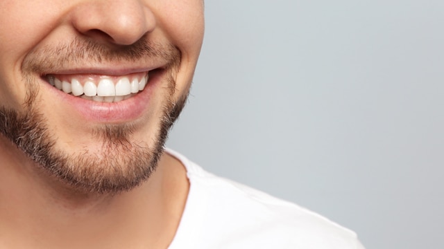 Close-up of a young man smiling in front of a gray wall