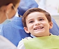 a smiling young boy is ready for his dental treatment and the dentist sits next to him