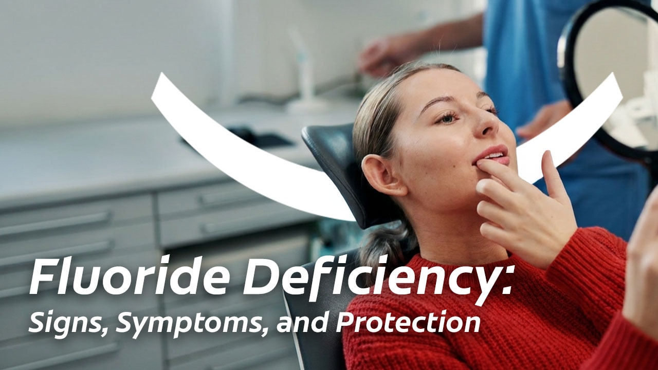 woman in a dental office examining her teeth with a handheld mirror. Overlay text reads: Fluoride Deficiency: Signs, Symptoms, and Protection