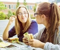 Two teen girls eating sandwiches outdoors