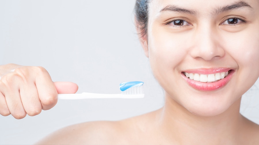 Close-up of a woman with beautiful white teeth applying whitening toothpaste