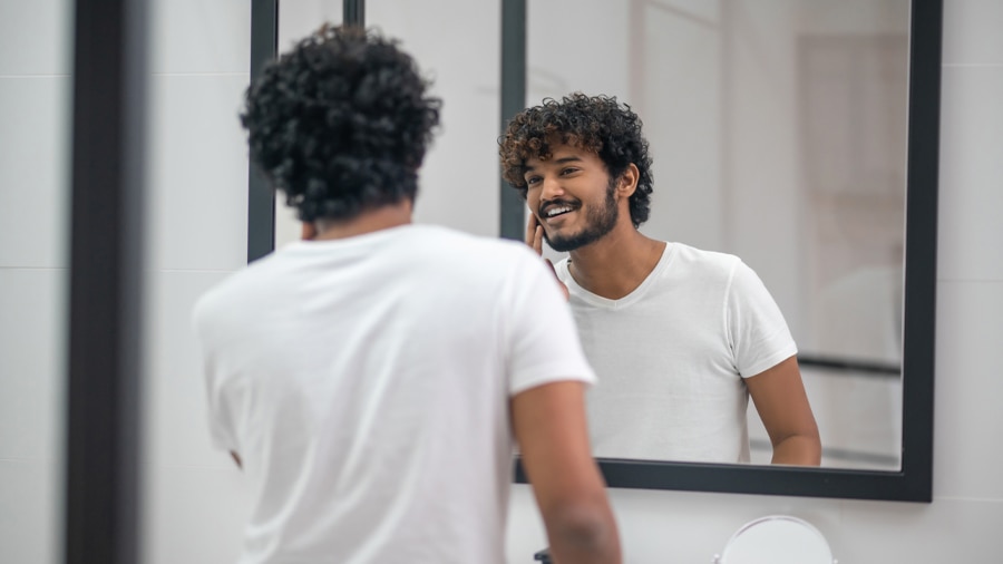 Young man happily looks in the mirror after using home remedies for gum pain