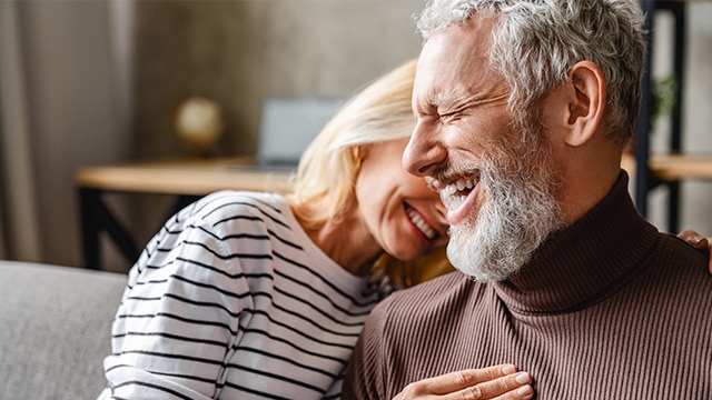 pareja de mediana edad feliz y riendo que se une mientras se relaja sentada en el sofá