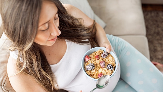 Vista superior de mujer embarazada feliz comiendo cereales con frutas para el desayuno en la cama en casa