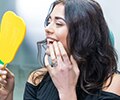 Young woman looking at her teeth using a hand-held mirror