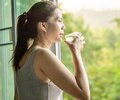 Asian woman drinking clean water in the morning next to the window with nature background