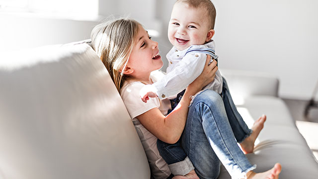 Little sister with her baby brother having good time at home while sitting on the sofa 