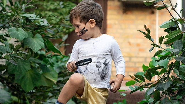 little boy with paint on his face, holding a magnifying glass, looking to side