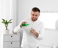 Young man pouring with mouthwash into small cup while standing in bathroom