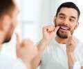 A man with dental floss cleaning teeth at a mirror in a bathroom