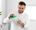 Young man pouring with mouthwash into small cup while standing in bathroom