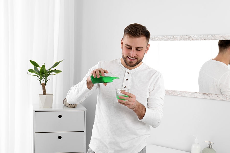 Young man pouring with mouthwash into small cup while standing in bathroom