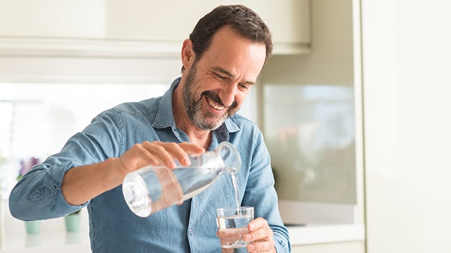 Hombre sirviéndose agua en un vaso mientras sonríe