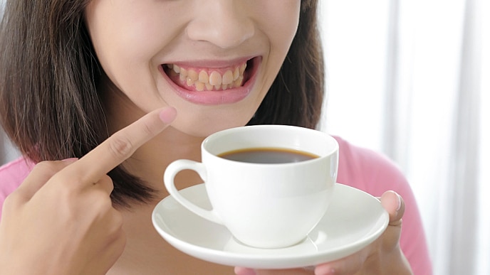 A woman showing stained teeth and holding a cup of coffee