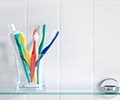 Toothbrushes and a tube of toothpaste in a glass cup on top of the bathroom shelf