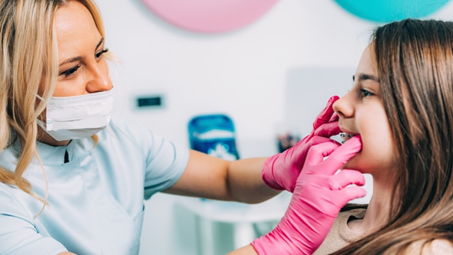 Female dentist examining the braces of a young female patient