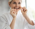 Women using a dental floss in front of the bathroom mirror