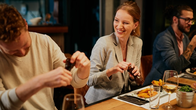 A man and woman sitting at a bar and talking and laughing while eating