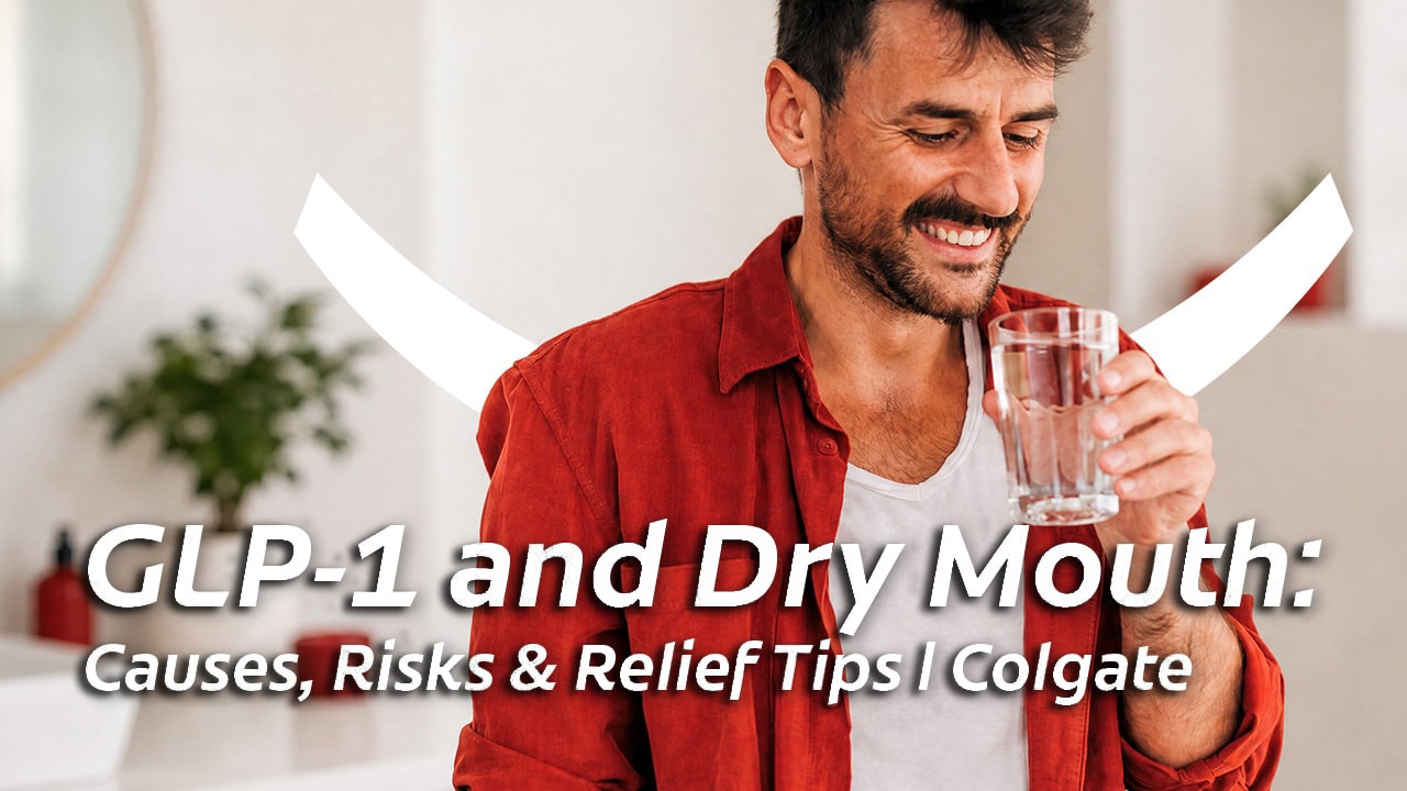 A smiling, dark-haired man in a white vest and red shirt, holding a glass of water up to his mouth to relieve GLP-1 dry mouth. 