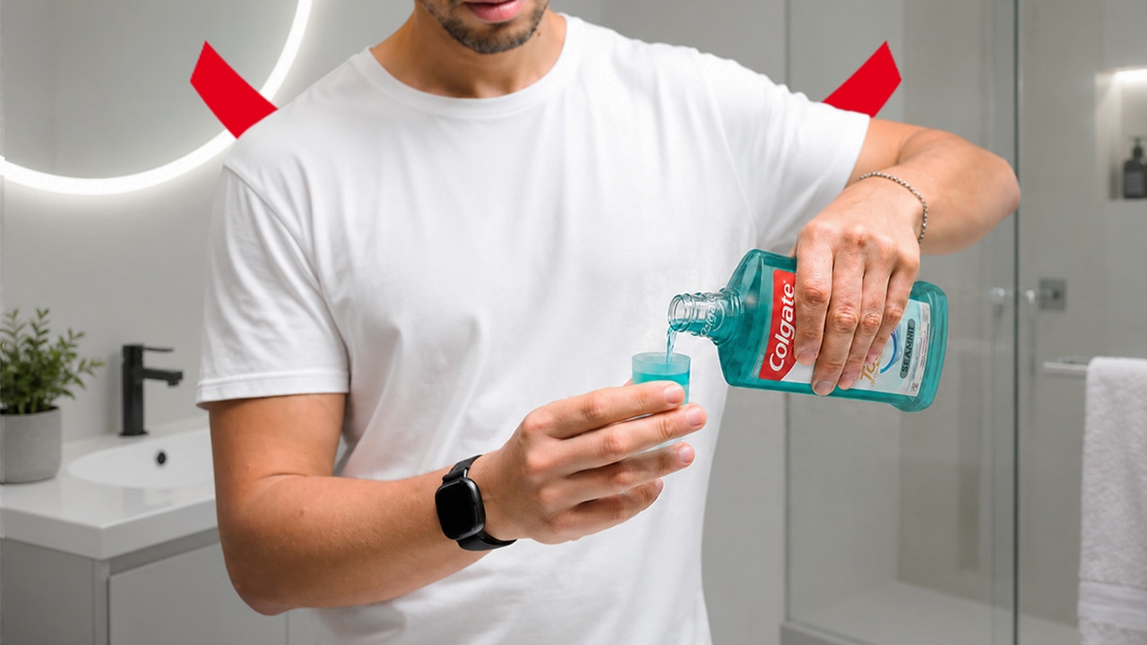 A man in a white t-shirt holding a bottle of Colgate mouthwash and pouring it into the cap to relieve GLP-1 bad breath. 