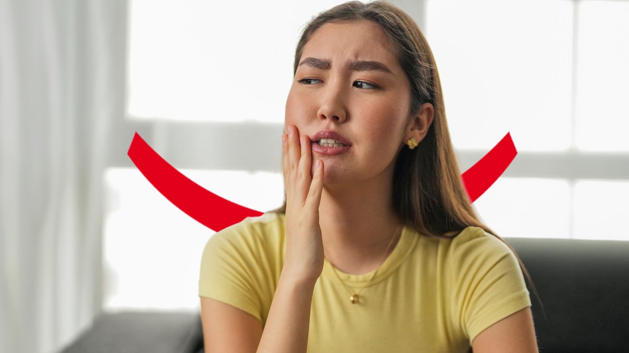 A blonde woman in a yellow t-shirt holding her hand to the side of her face and looking uncomfortable due to GLP-1 mouth sores.